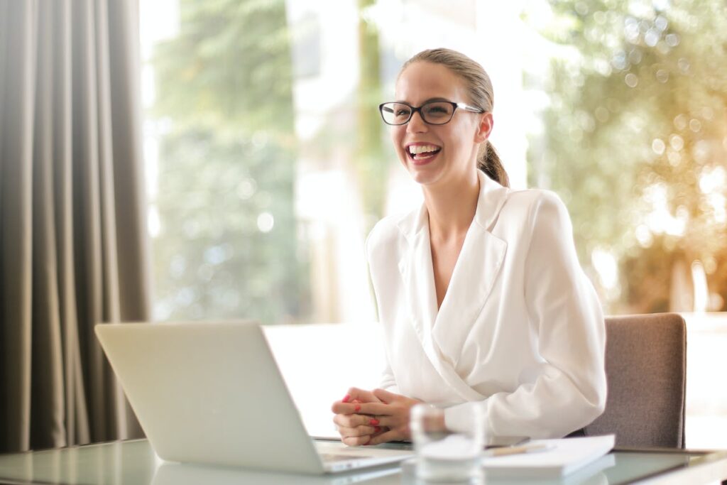 Smiling businesswoman using a laptop, symbolizing the customer satisfaction guaranteed by KAMINOWEB's reliable and fast WordPress hosting services.