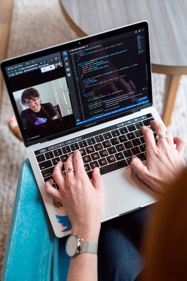 Hands typing on a laptop with code on the screen and a video call in the background, illustrating KAMINOWEB's dedicated WordPress support and proactive service.